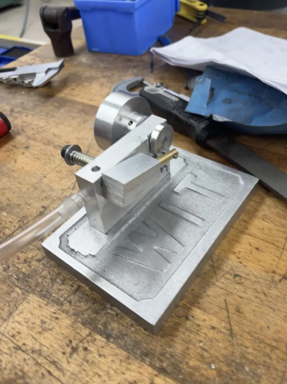 The finished pneumatic air piston with its flywheel, air tubing, and cast mounting plate on a workbench.